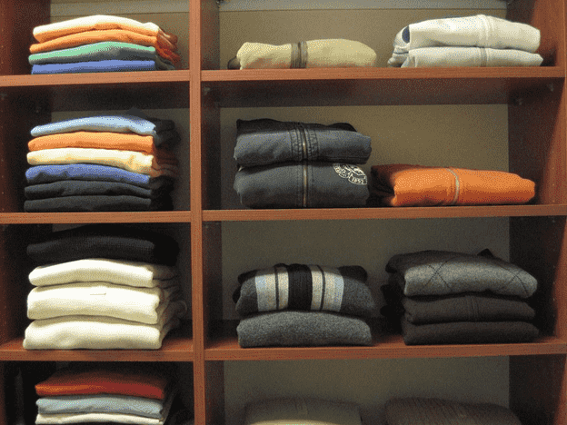 Folded sweaters neatly stacked on wooden closet shelves